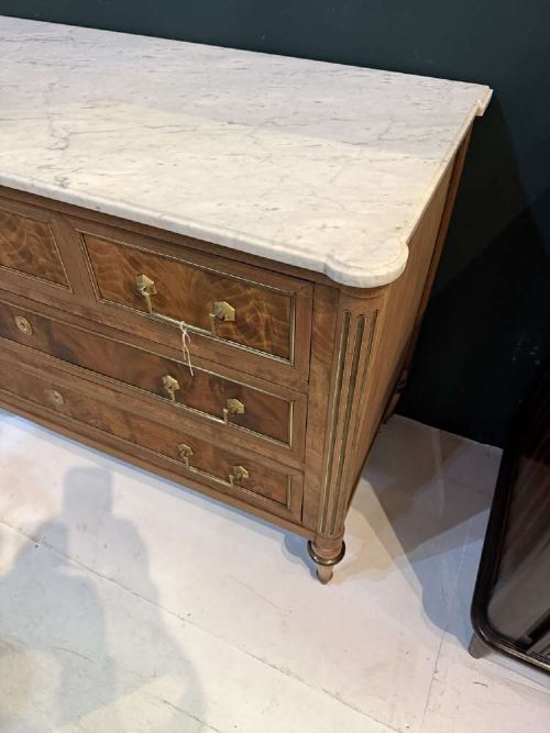 A nineteenth-century Louis XVI style scrubbed mahogany commode featuring three drawers, brass handles, keyhole escutcheons, turned tapered legs, and a fitted white marble top. View II