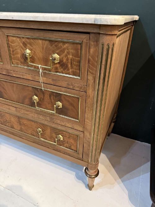 A nineteenth-century Louis XVI style scrubbed mahogany commode featuring three drawers, brass handles, keyhole escutcheons, turned tapered legs, and a fitted white marble top. View III