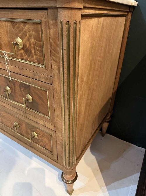 A nineteenth-century Louis XVI style scrubbed mahogany commode featuring three drawers, brass handles, keyhole escutcheons, turned tapered legs, and a fitted white marble top. View IV