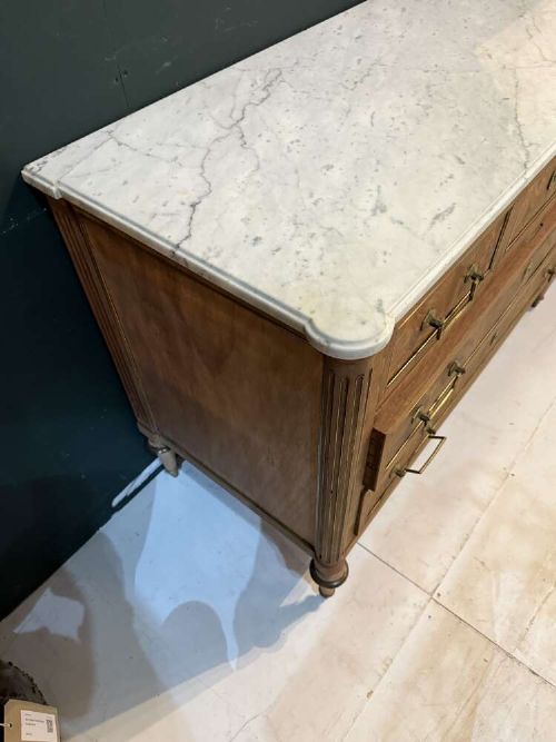 A nineteenth-century Louis XVI style scrubbed mahogany commode featuring three drawers, brass handles, keyhole escutcheons, turned tapered legs, and a fitted white marble top. View V