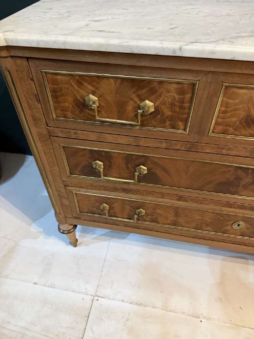 A nineteenth-century Louis XVI style scrubbed mahogany commode featuring three drawers, brass handles, keyhole escutcheons, turned tapered legs, and a fitted white marble top. View VII
