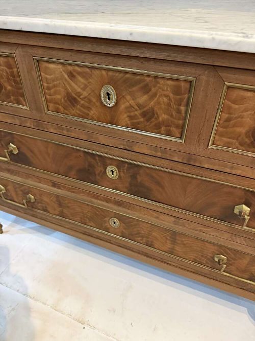 A nineteenth-century Louis XVI style scrubbed mahogany commode featuring three drawers, brass handles, keyhole escutcheons, turned tapered legs, and a fitted white marble top. View VIII
