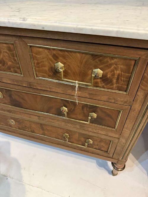A nineteenth-century Louis XVI style scrubbed mahogany commode featuring three drawers, brass handles, keyhole escutcheons, turned tapered legs, and a fitted white marble top. View IX