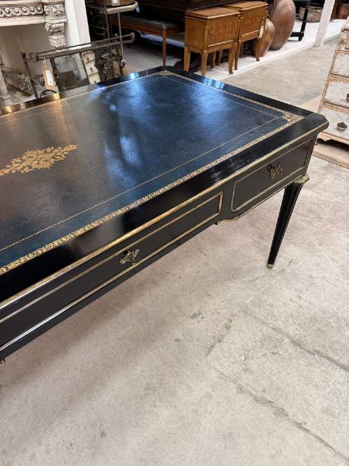 A 19th-century French ebonised writing desk with a black leather inset top, gilt-tooled border, three frieze drawers, brass mounts, and tapered fluted legs. View IV