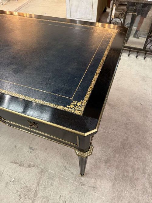 A 19th-century French ebonised writing desk with a black leather inset top, gilt-tooled border, three frieze drawers, brass mounts, and tapered fluted legs. View V