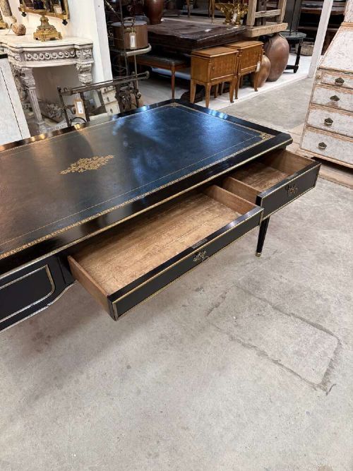 A 19th-century French ebonised writing desk with a black leather inset top, gilt-tooled border, three frieze drawers, brass mounts, and tapered fluted legs. View VI