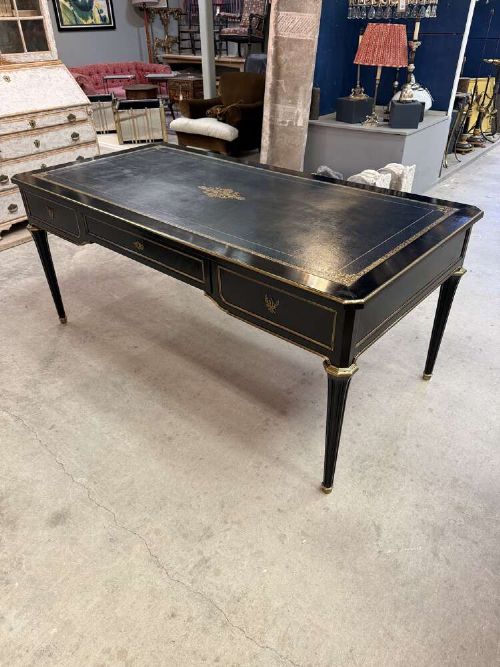 A 19th-century French ebonised writing desk with a black leather inset top, gilt-tooled border, three frieze drawers, brass mounts, and tapered fluted legs. View X
