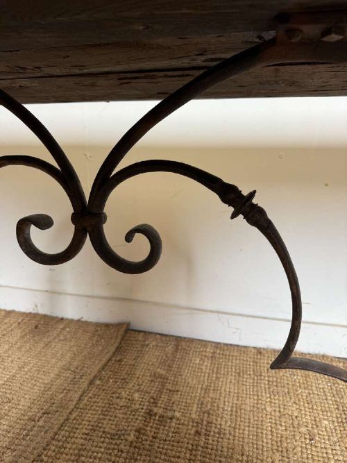 A long scrubbed oak refectory table with carved trestle legs connected by a central curved wrought iron scroll stretcher. View X