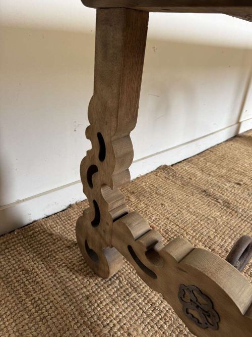 A long scrubbed oak refectory table with carved trestle legs connected by a central curved wrought iron scroll stretcher. View XII