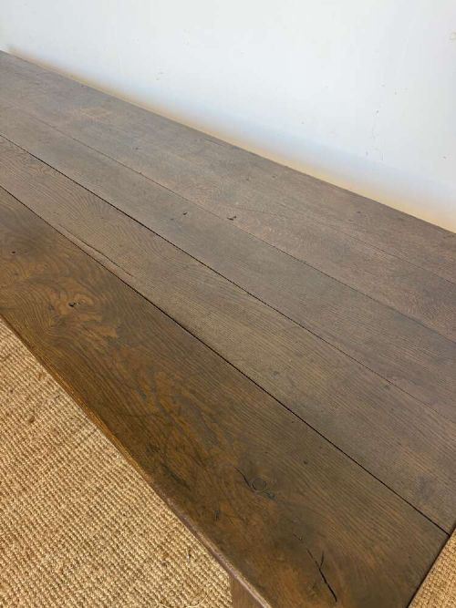 A long dark oak French farmhouse dining table featuring a plank top surface and four tapered square legs. View IV