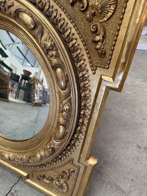 A square carved giltwood frame with detailed corner spandrels housing a central round convex glass mirror. View III