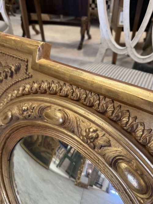 A square carved giltwood frame with detailed corner spandrels housing a central round convex glass mirror. View V