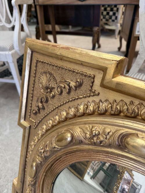 A square carved giltwood frame with detailed corner spandrels housing a central round convex glass mirror. View VI