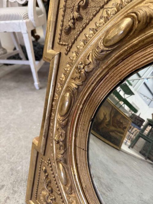 A square carved giltwood frame with detailed corner spandrels housing a central round convex glass mirror. View VII