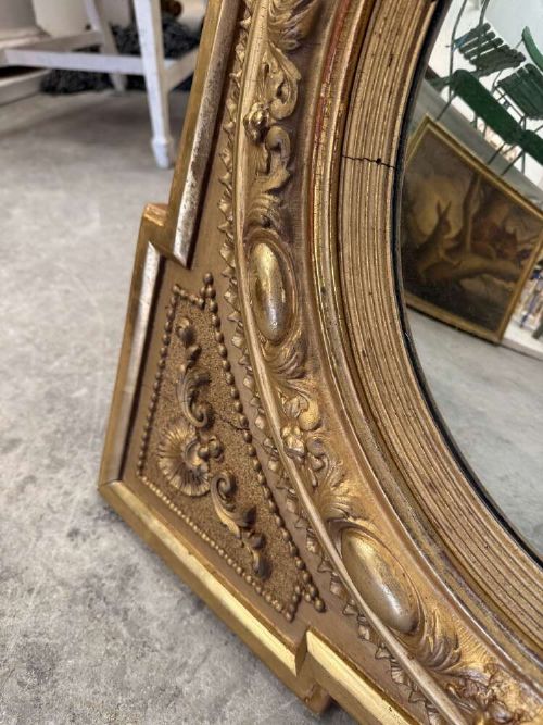 A square carved giltwood frame with detailed corner spandrels housing a central round convex glass mirror. View VIII
