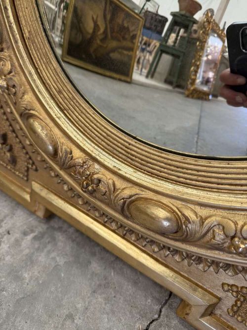 A square carved giltwood frame with detailed corner spandrels housing a central round convex glass mirror. View IX