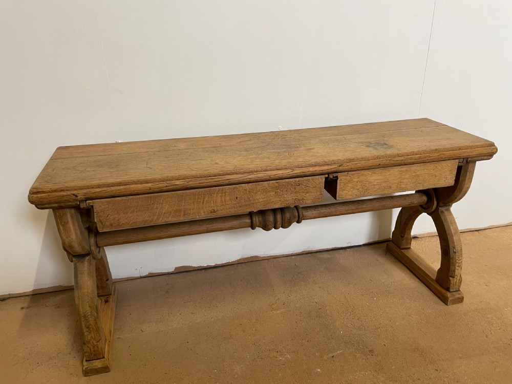 A Victorian oak window seat featuring arched Gothic Revival end legs, two frieze drawers, and a central turned stretcher.