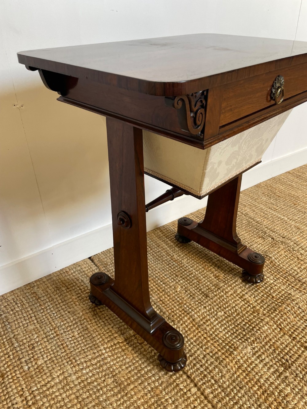 A Victorian rosewood work table featuring a single drawer with a brass ring handle, carved side brackets, and an upholstered fabric well beneath. View II