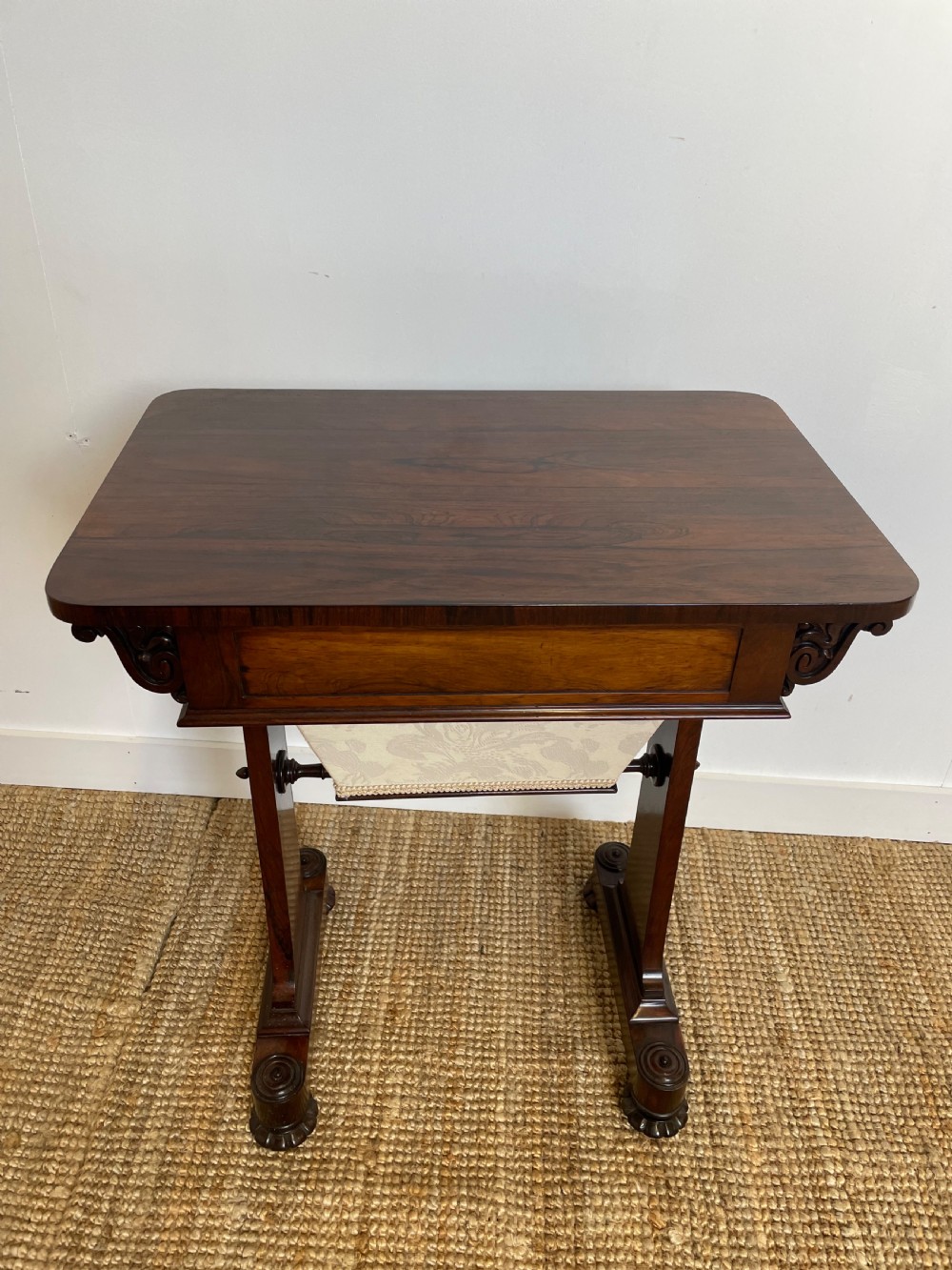 A Victorian rosewood work table featuring a single drawer with a brass ring handle, carved side brackets, and an upholstered fabric well beneath. View VI