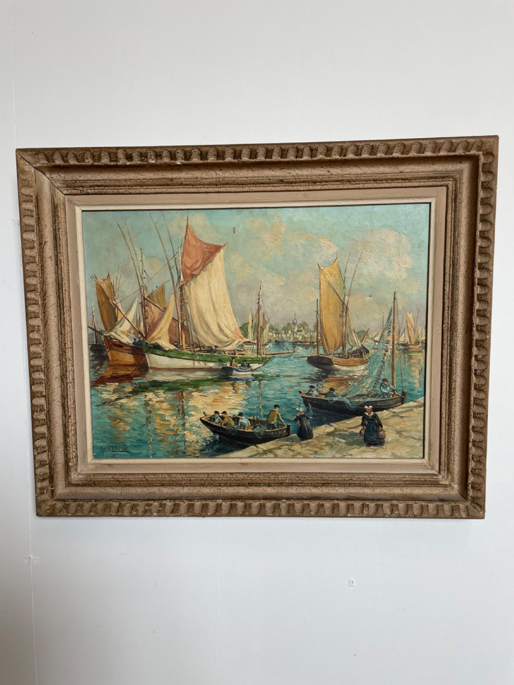 An oil painting on canvas depicting traditional fishing boats docked in a harbour alongside figures on a stone quay, enclosed in a carved wooden frame.