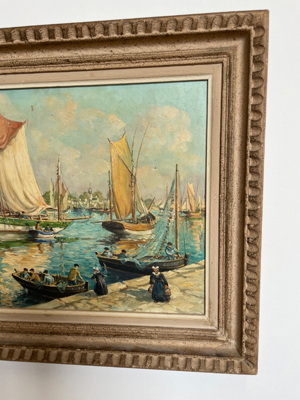 An oil painting on canvas depicting traditional fishing boats docked in a harbour alongside figures on a stone quay, enclosed in a carved wooden frame. View II