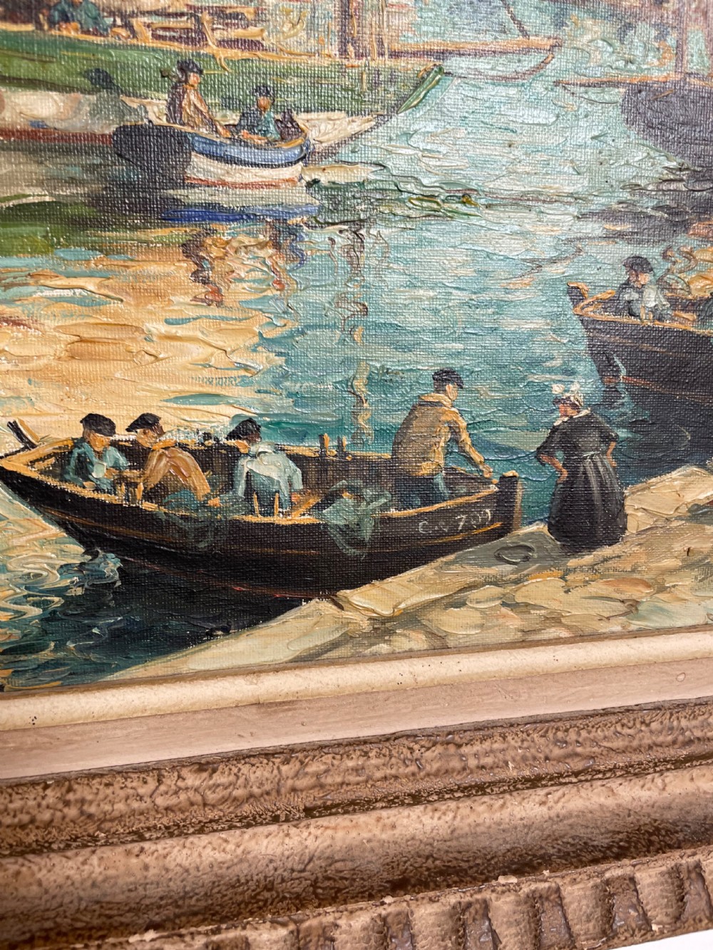An oil painting on canvas depicting traditional fishing boats docked in a harbour alongside figures on a stone quay, enclosed in a carved wooden frame. View V