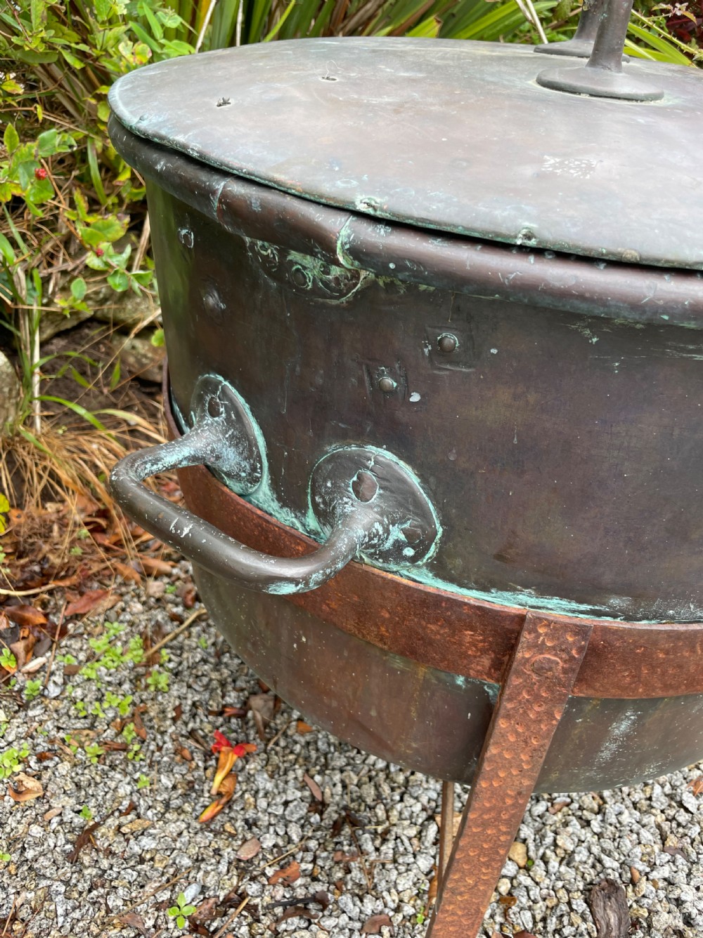 A large lidded copper log bin featuring riveted side handles, a flat lid with a central handle, and a raised iron support stand. View VI