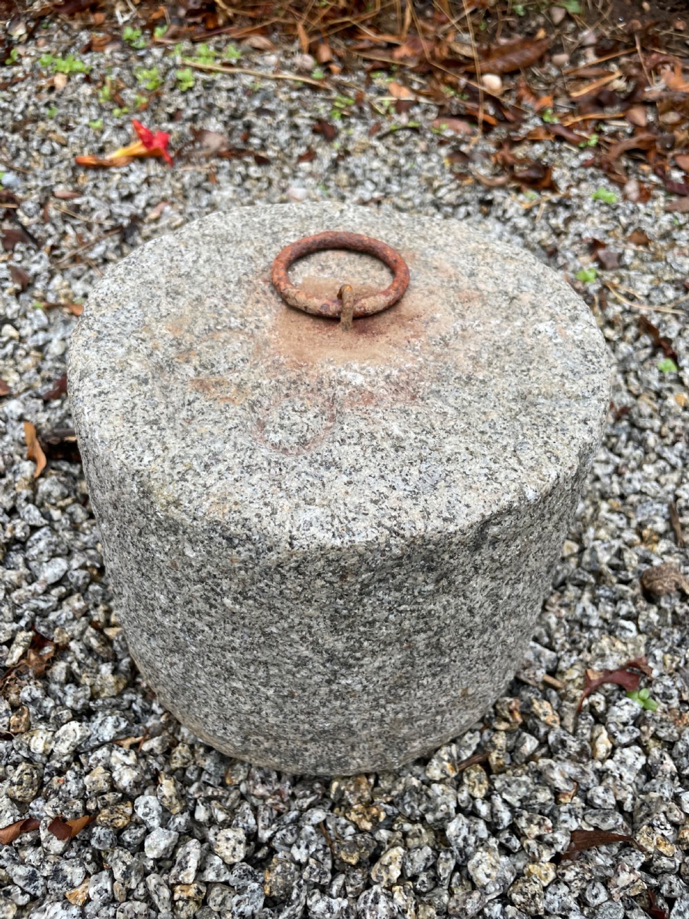 A cylindrical antique granite tethering block featuring a rusted iron ring set into the top centre surface. View II