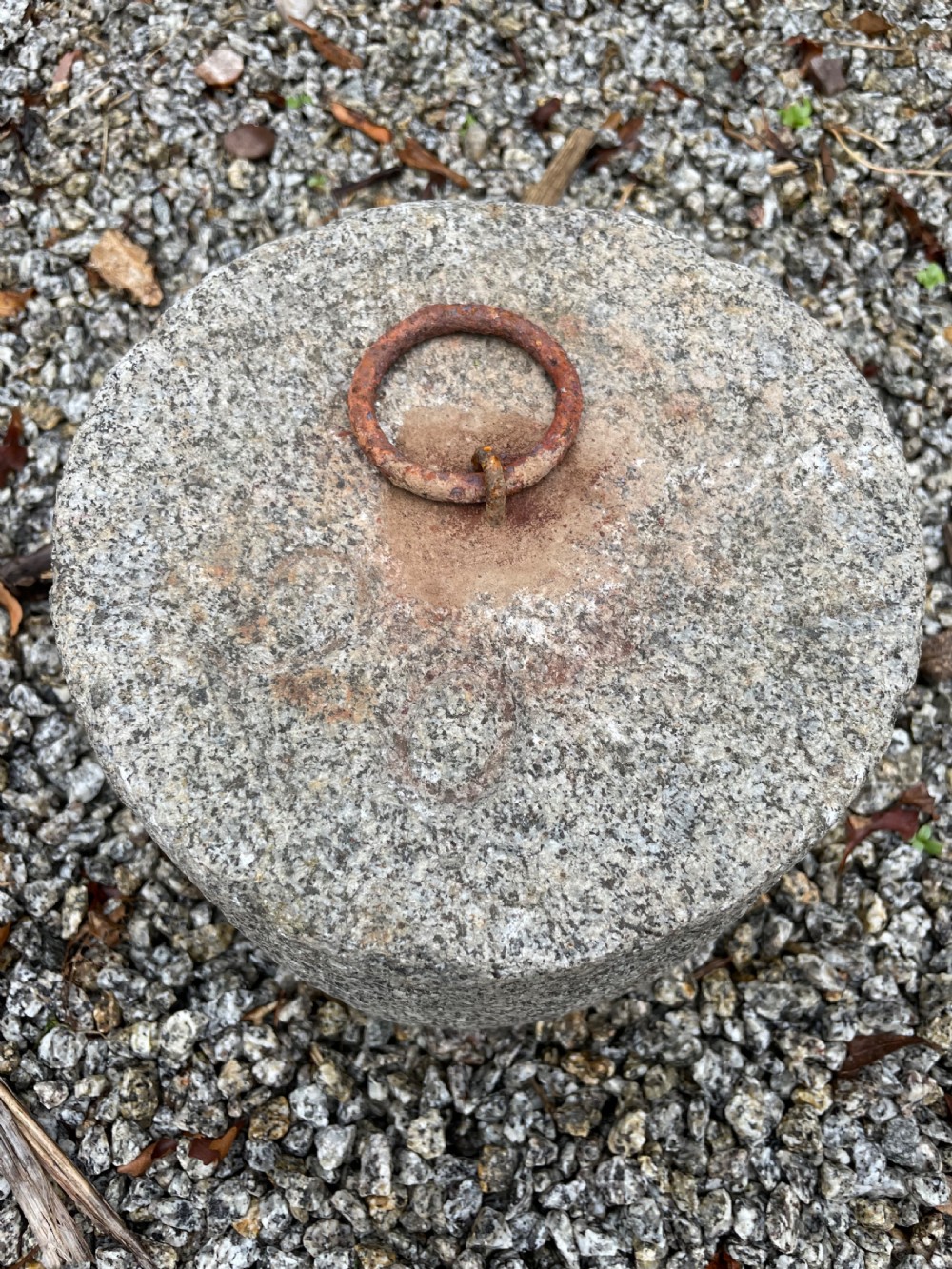 A cylindrical antique granite tethering block featuring a rusted iron ring set into the top centre surface. View III