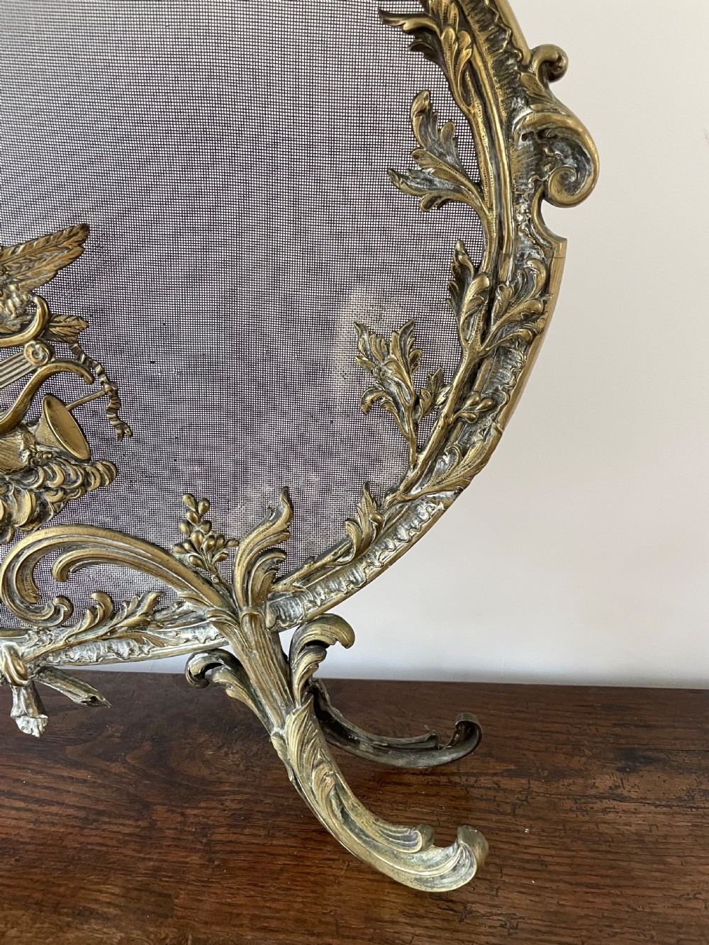 An ornate antique brass fire screen featuring pierced scrollwork, a central lyre and bird motif, and a wire mesh panel. View II