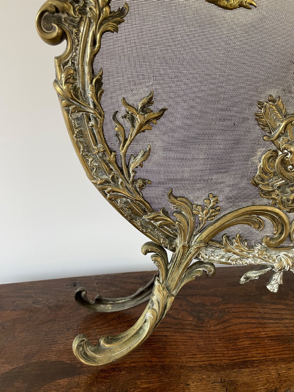 An ornate antique brass fire screen featuring pierced scrollwork, a central lyre and bird motif, and a wire mesh panel. View IV