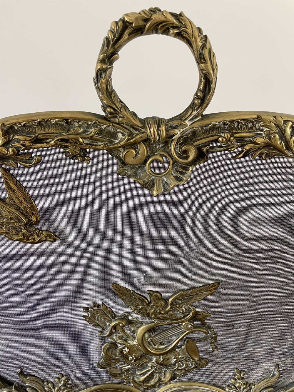 An ornate antique brass fire screen featuring pierced scrollwork, a central lyre and bird motif, and a wire mesh panel. View VI