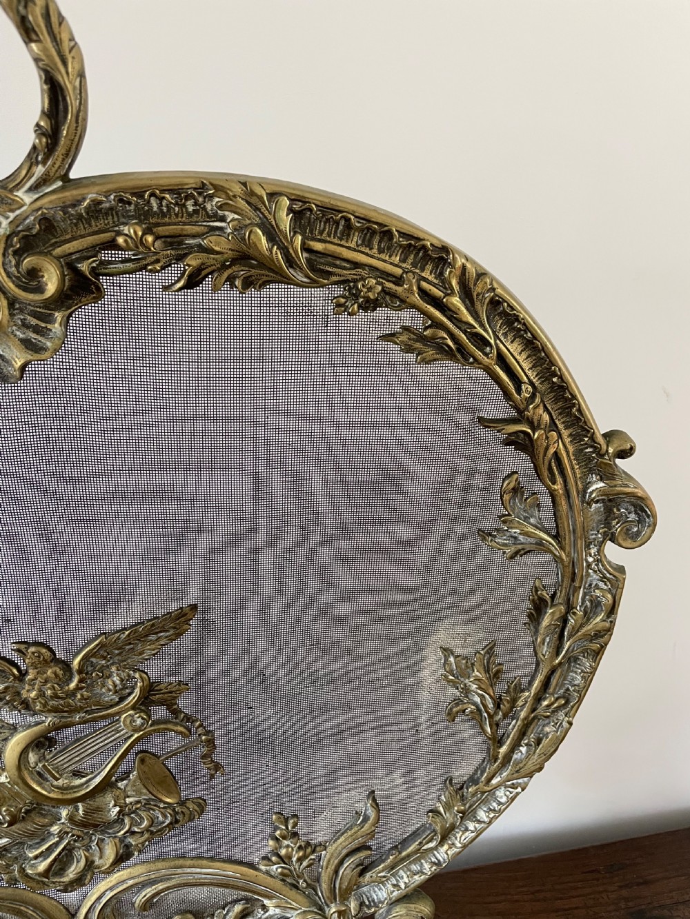 An ornate antique brass fire screen featuring pierced scrollwork, a central lyre and bird motif, and a wire mesh panel. View VII