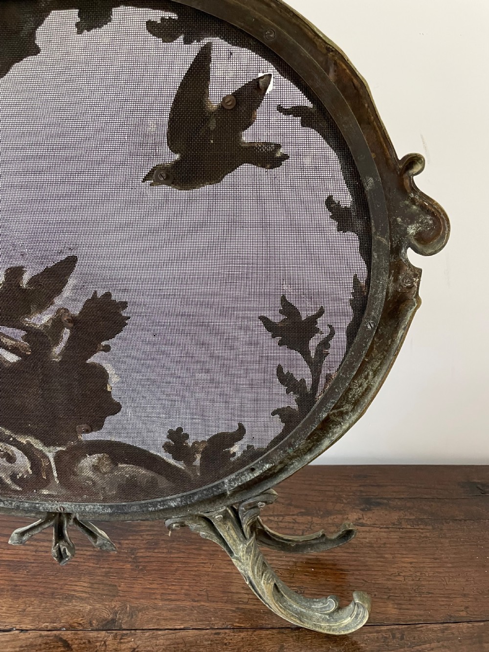 An ornate antique brass fire screen featuring pierced scrollwork, a central lyre and bird motif, and a wire mesh panel. View VIII