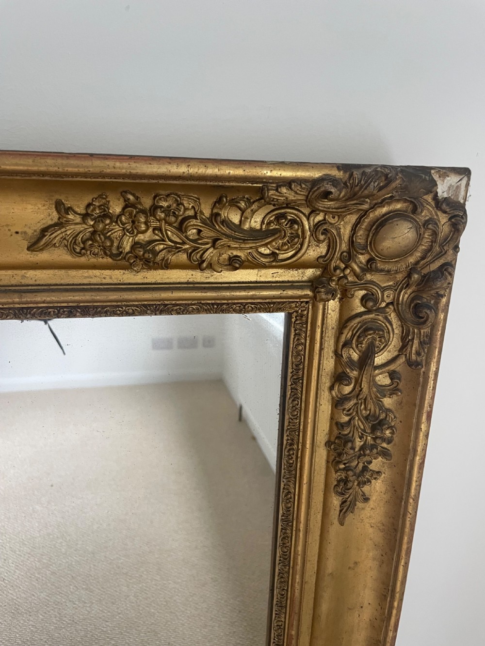 A large rectangular antique overmantel mirror featuring a gilded frame embellished with gesso scrollwork, floral motifs, and a central cartouche top emblem. View IV