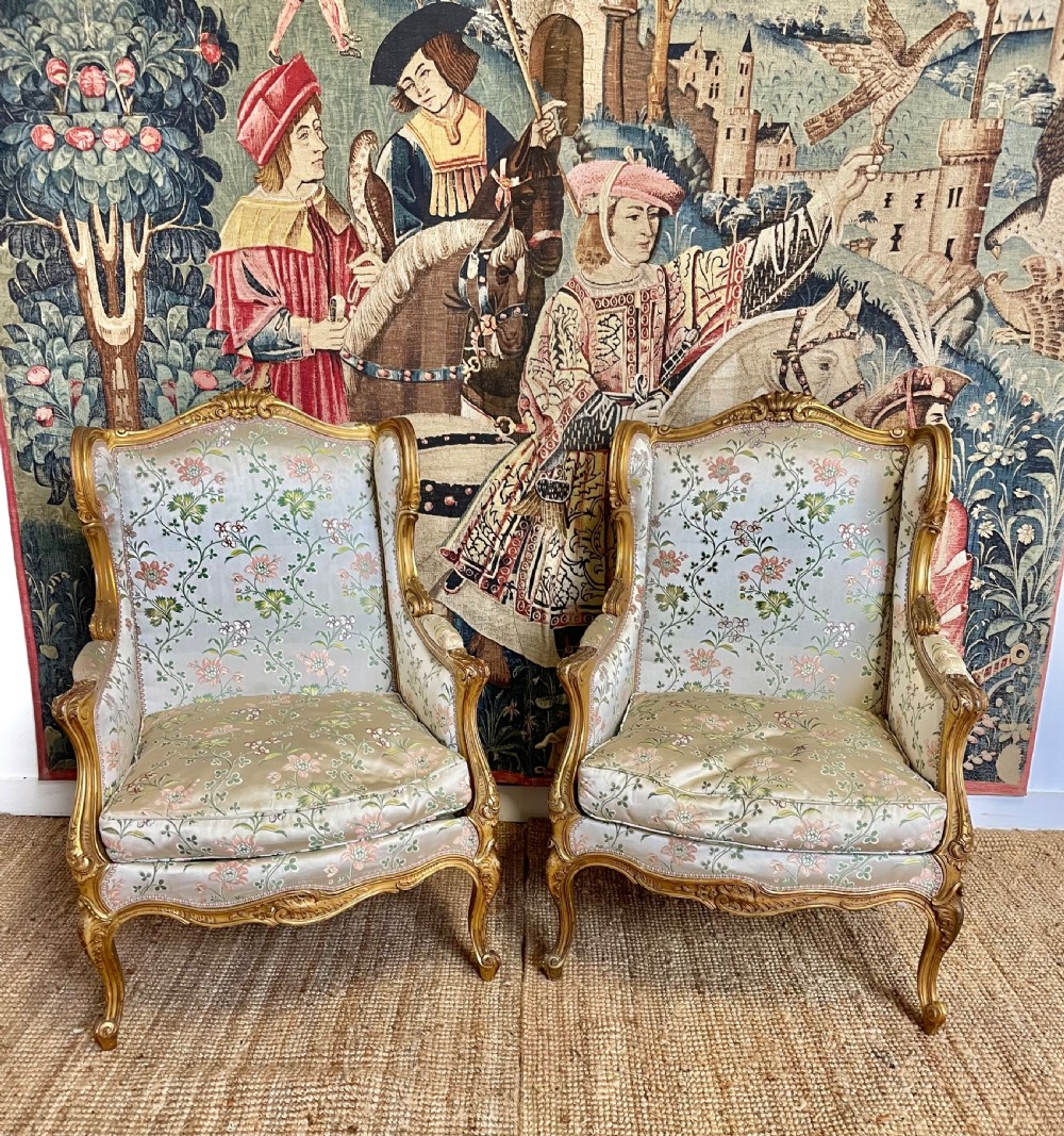 A pair of carved gilt wood fauteuil armchairs upholstered in patterned floral silk fabric.