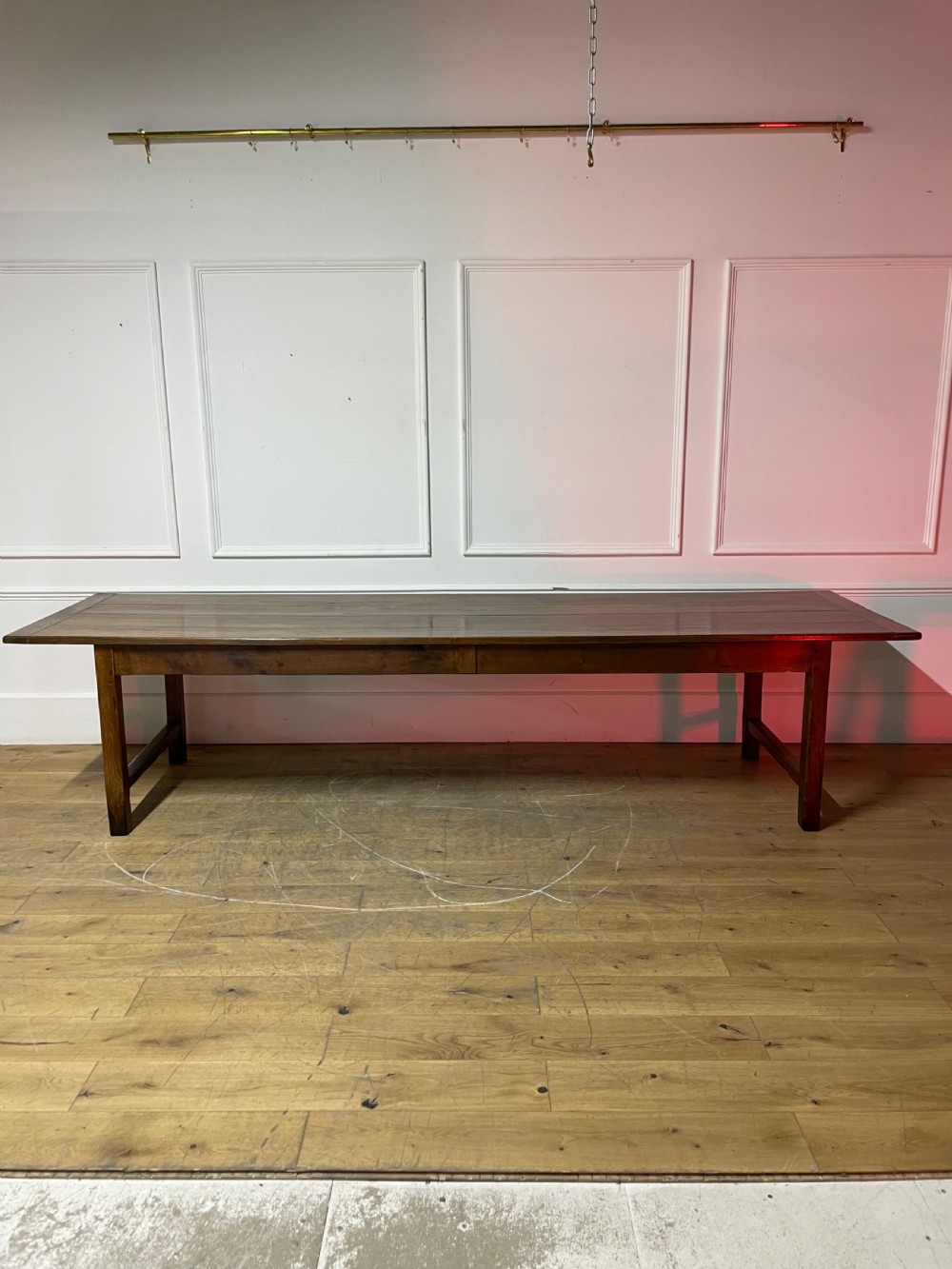 A long, antique oak farmhouse dining table featuring a planked timber top and straight wooden legs joined by side stretchers.