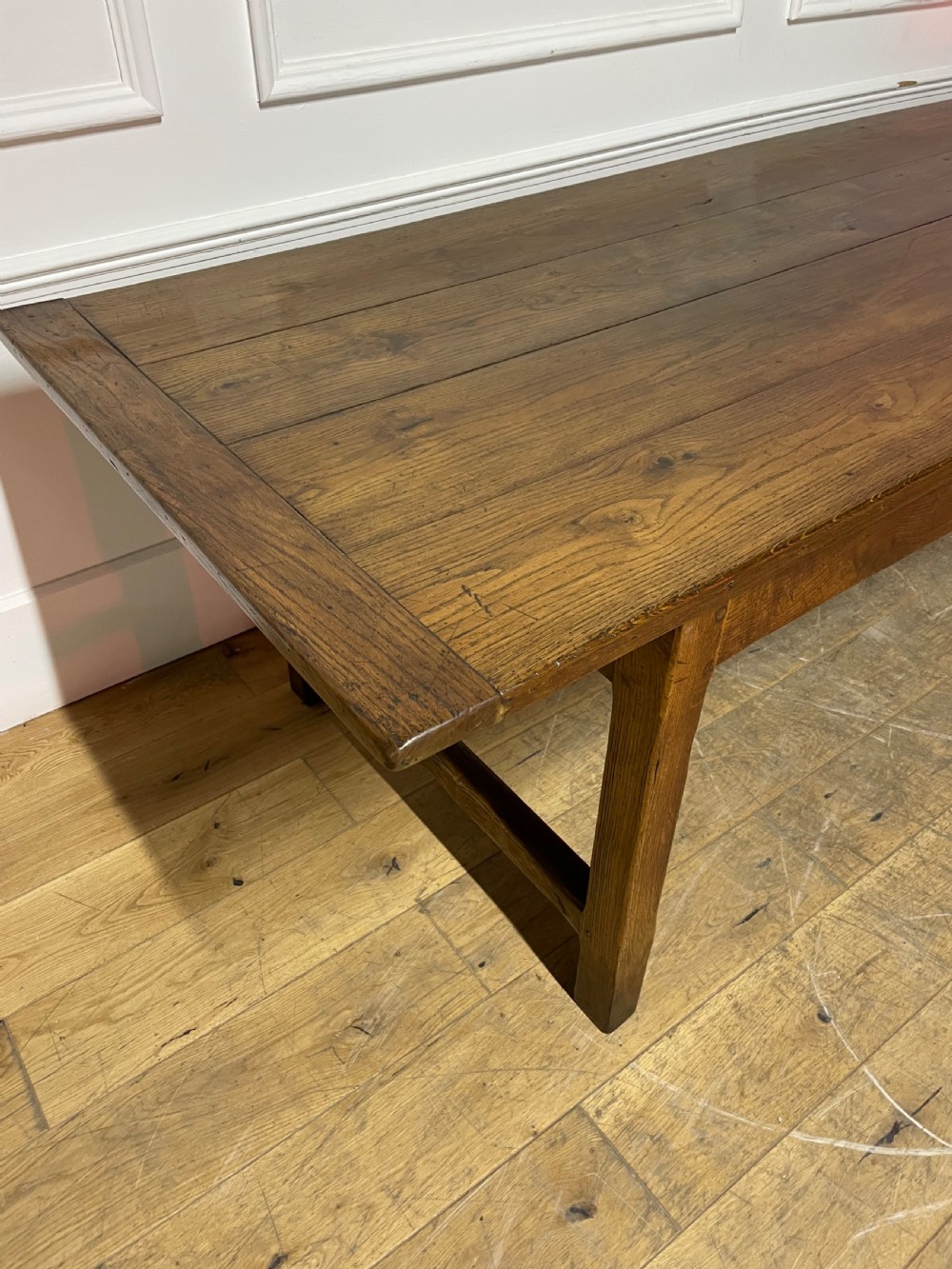 A long, antique oak farmhouse dining table featuring a planked timber top and straight wooden legs joined by side stretchers. View II