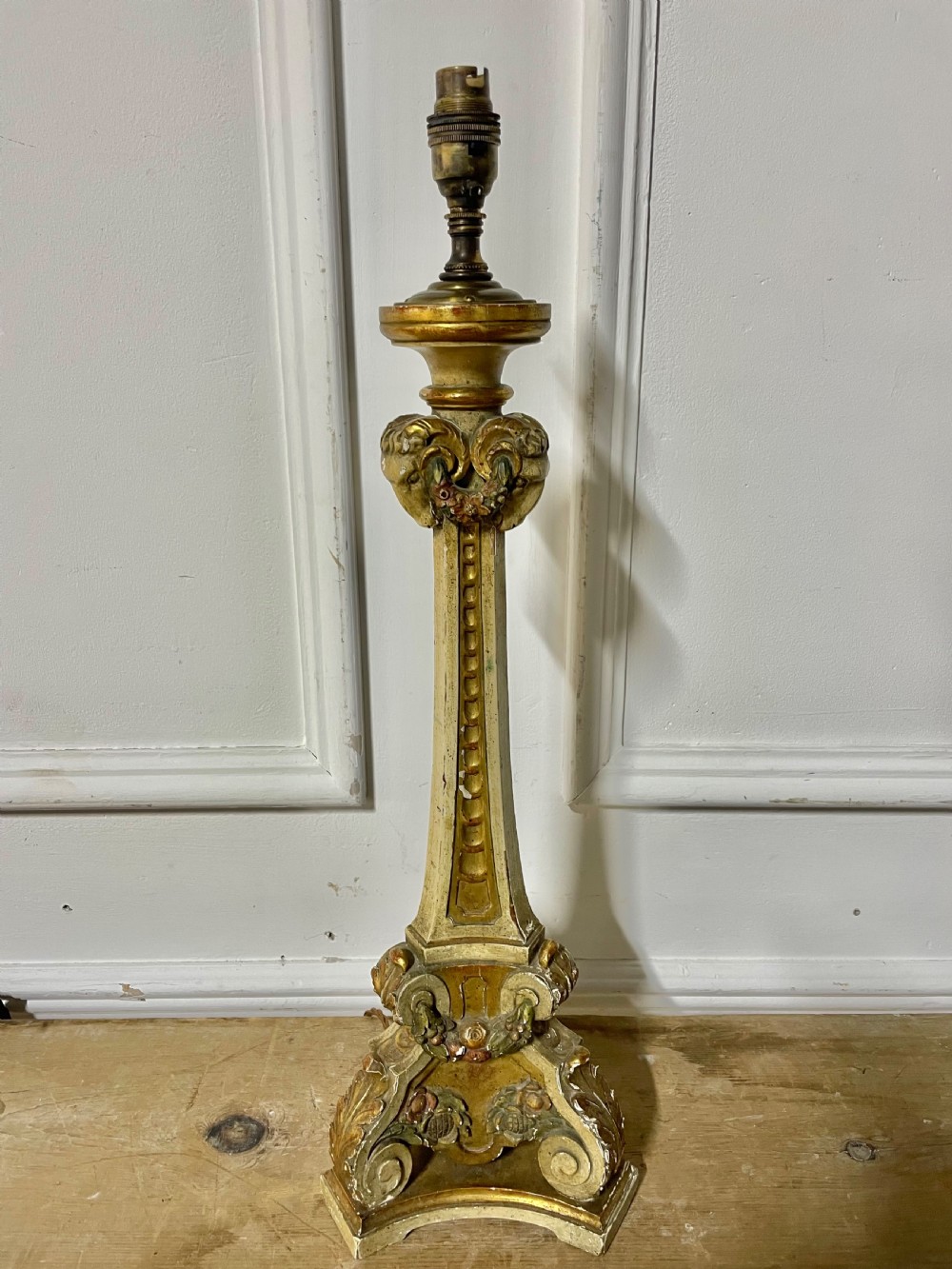 A tall, carved giltwood and cream painted table lamp base featuring neoclassical scrollwork and floral swags.