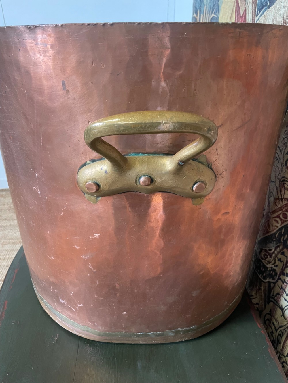 A large cylindrical copper log bin featuring two cast brass side handles and a hammered metal finish. View II
