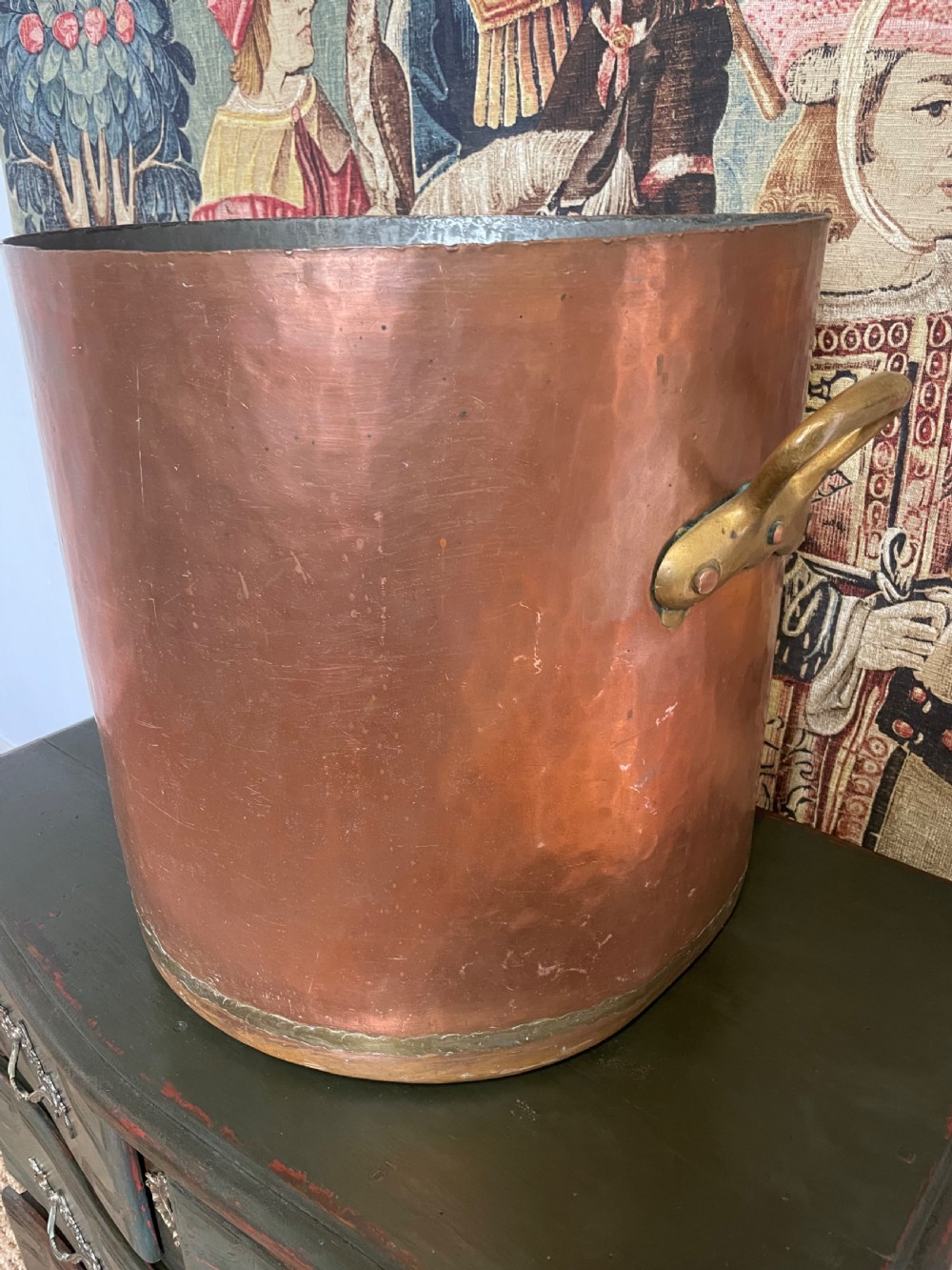 A large cylindrical copper log bin featuring two cast brass side handles and a hammered metal finish. View III
