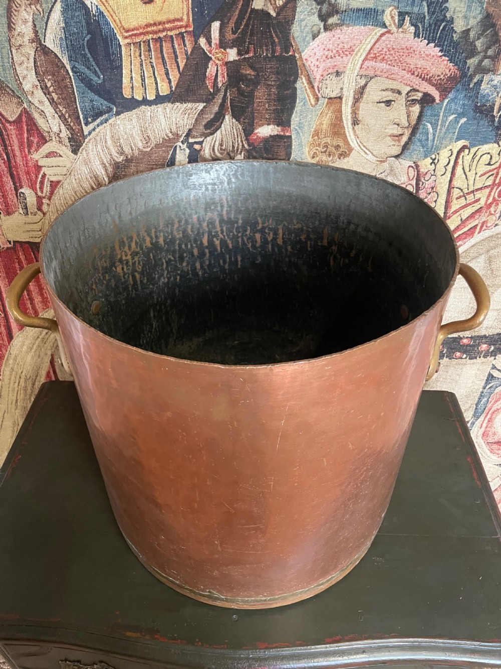 A large cylindrical copper log bin featuring two cast brass side handles and a hammered metal finish. View V