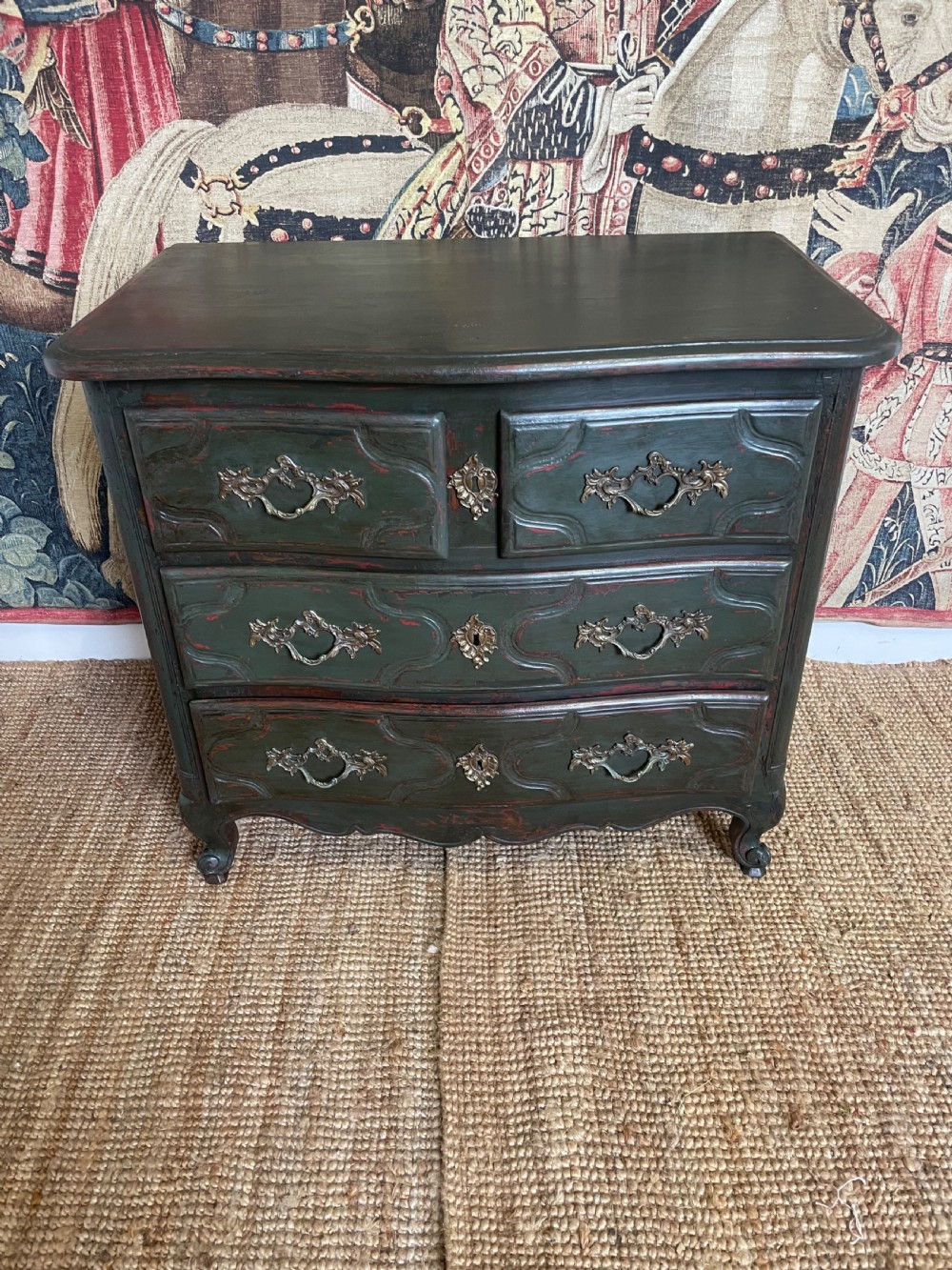 A dark green painted French commode chest of drawers featuring moulded panels, distressed finish, and decorative brass handles.