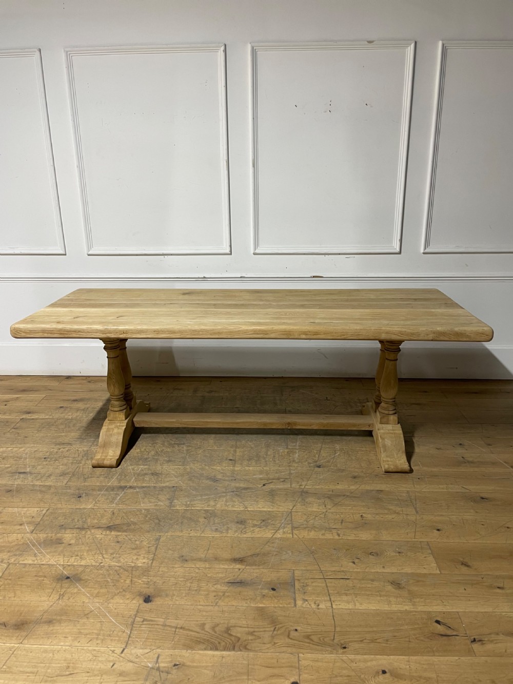 A long rectangular scrubbed oak refectory table featuring turned pedestal supports and a central stretcher.