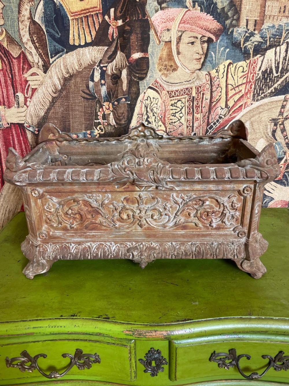 A rectangular cast iron planter trough featuring ornate relief scrollwork, foliate motifs, and a weathered rust patina.