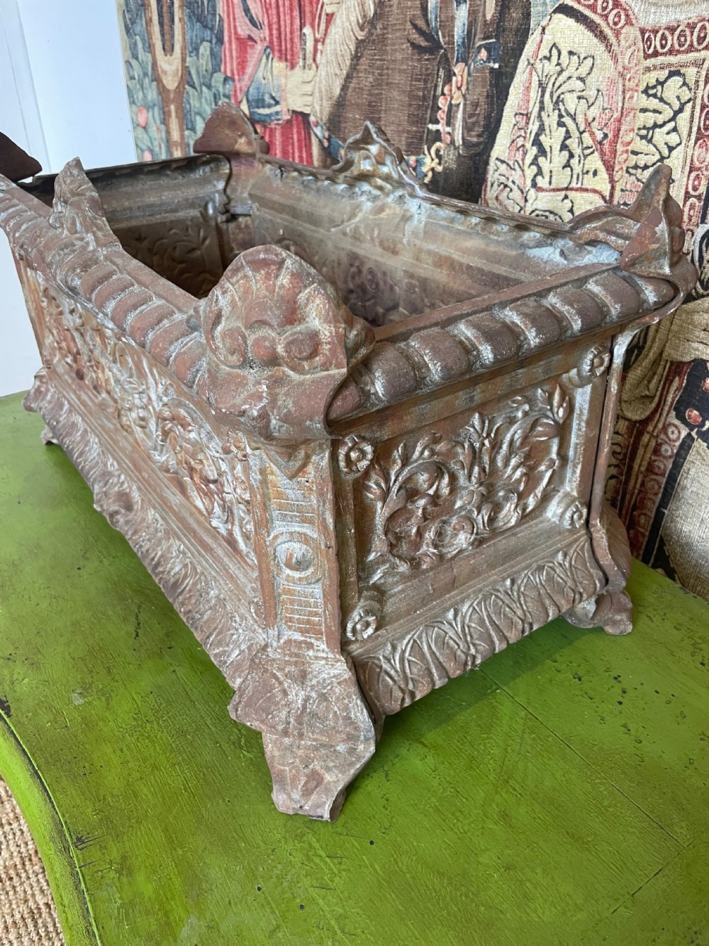 A rectangular cast iron planter trough featuring ornate relief scrollwork, foliate motifs, and a weathered rust patina. View III