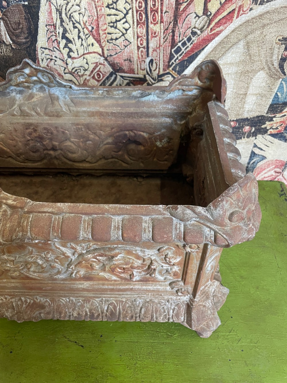 A rectangular cast iron planter trough featuring ornate relief scrollwork, foliate motifs, and a weathered rust patina. View V