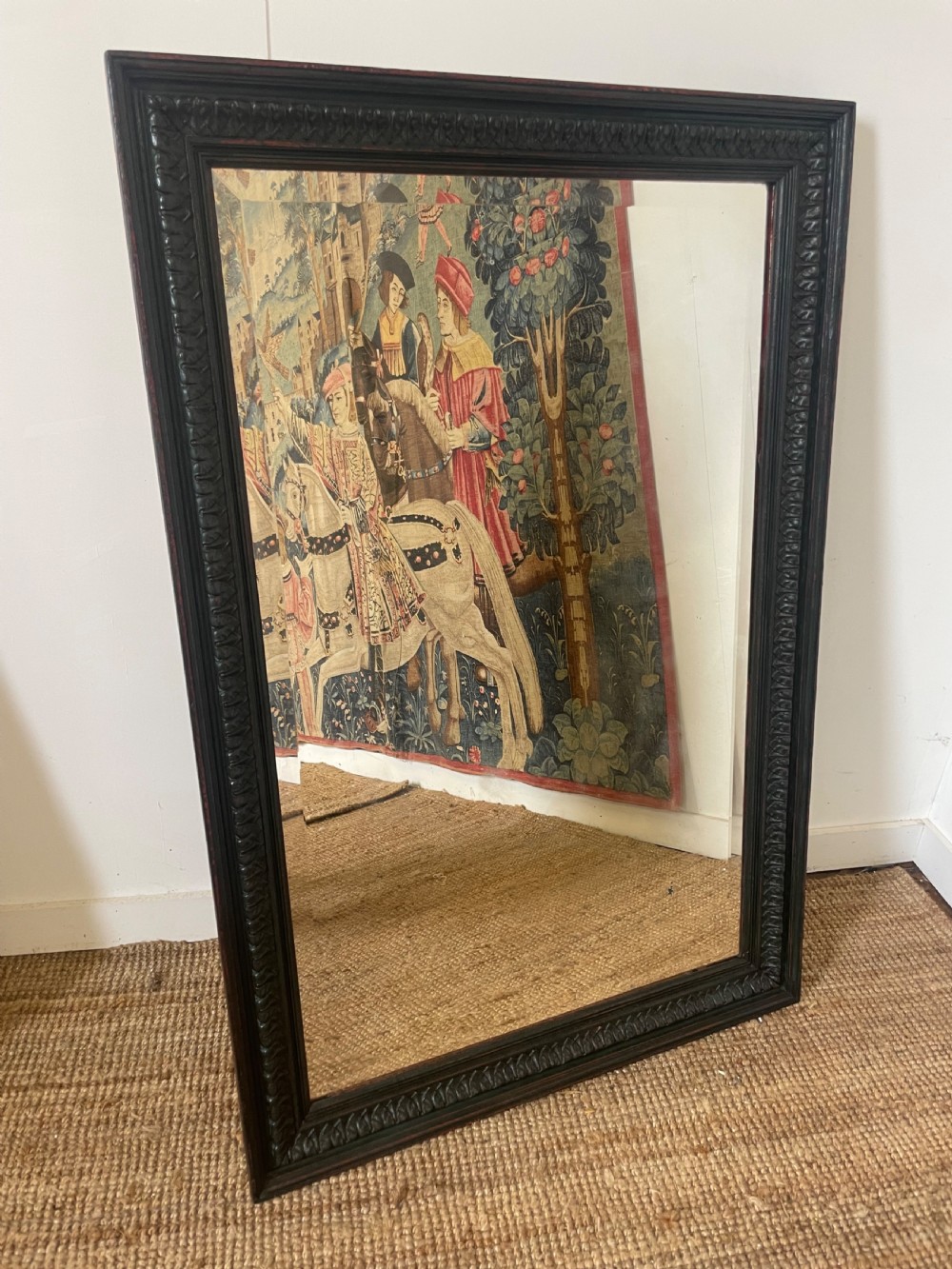 A large rectangular wall mirror with a dark, distressed carved wooden frame resting against a white wall.