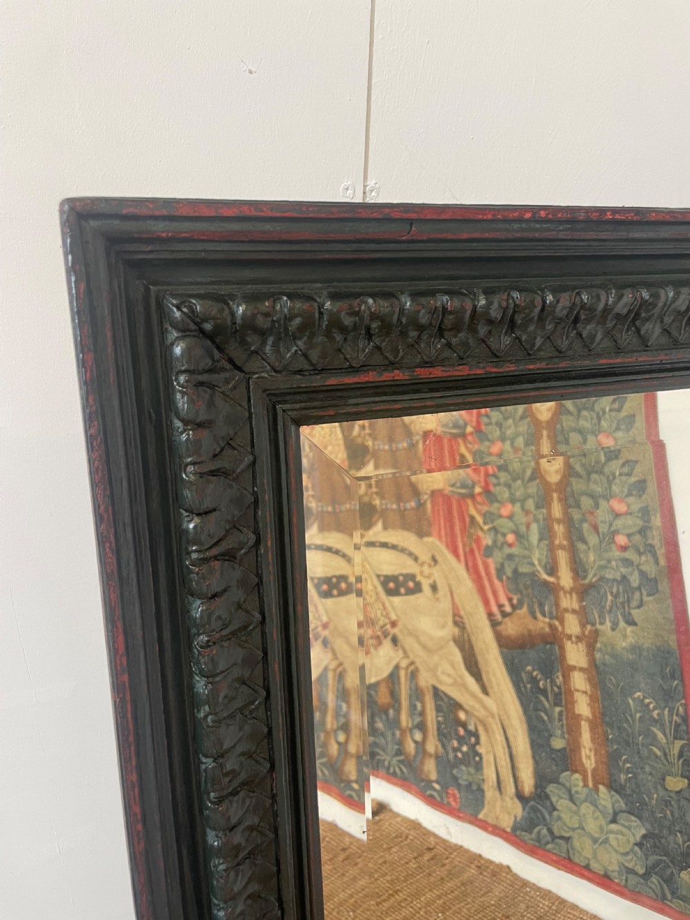 A large rectangular wall mirror with a dark, distressed carved wooden frame resting against a white wall. View II