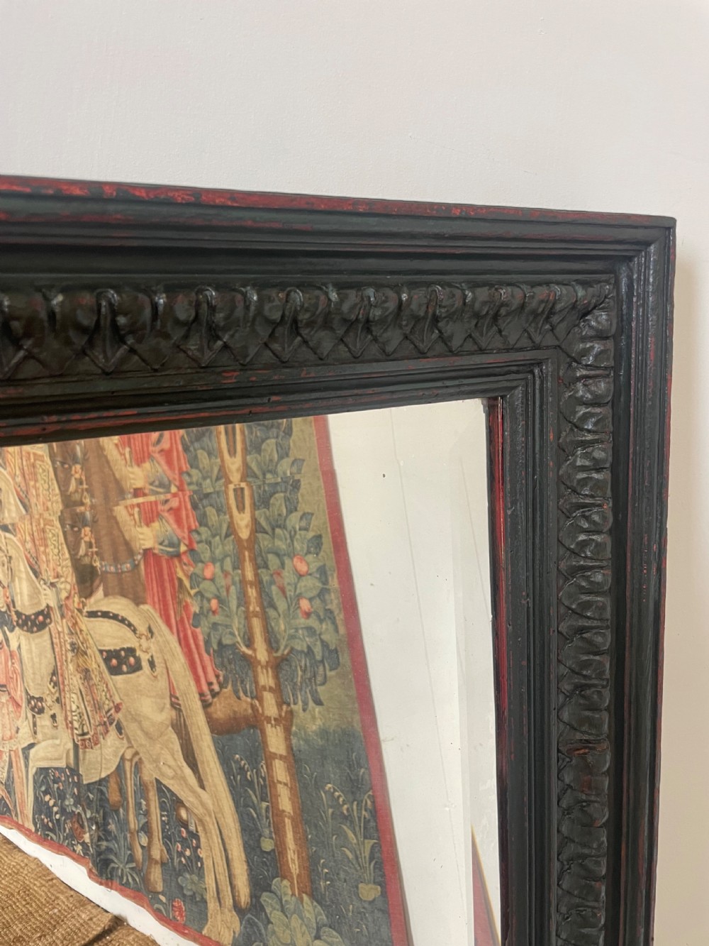 A large rectangular wall mirror with a dark, distressed carved wooden frame resting against a white wall. View III